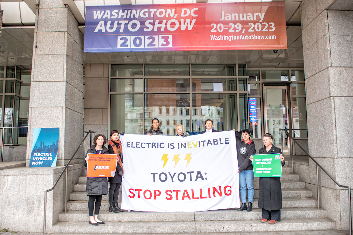 7 people stand around a sign that reads, 